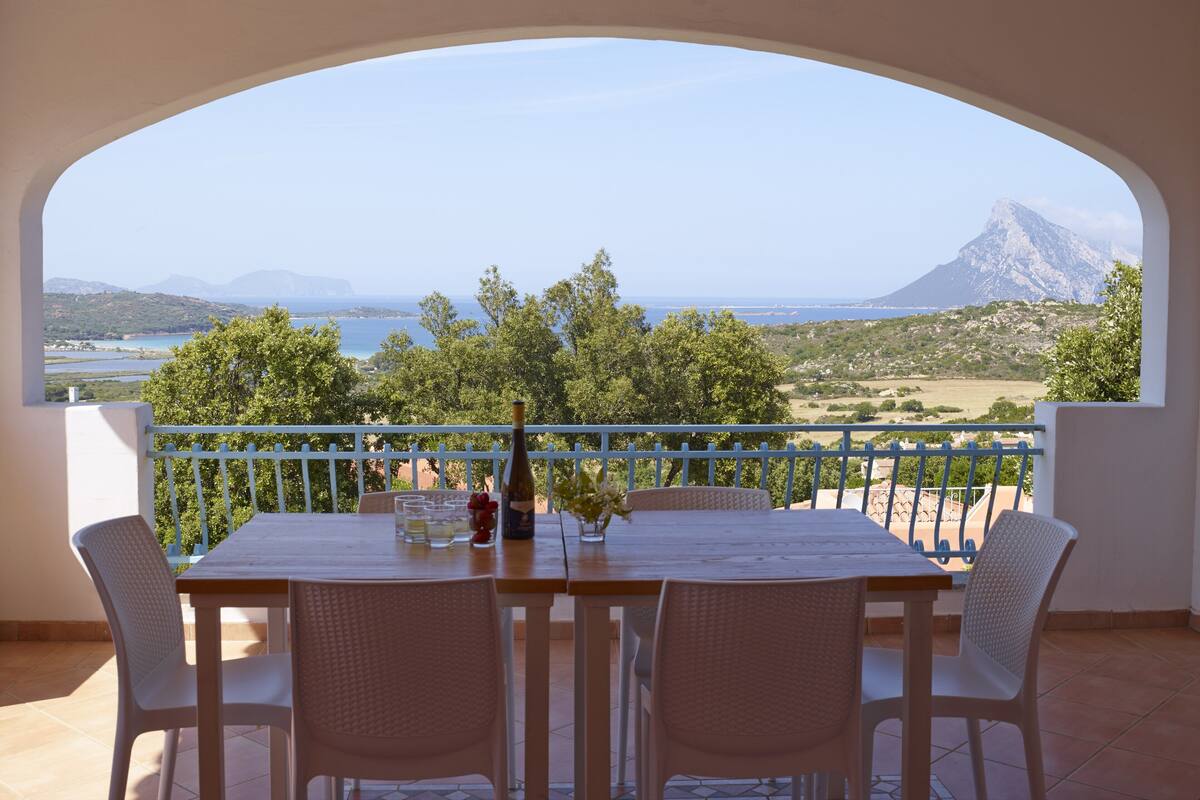 A balcony with a table and chairs, overlooking a scenic landscape with mountains and a body of water.
