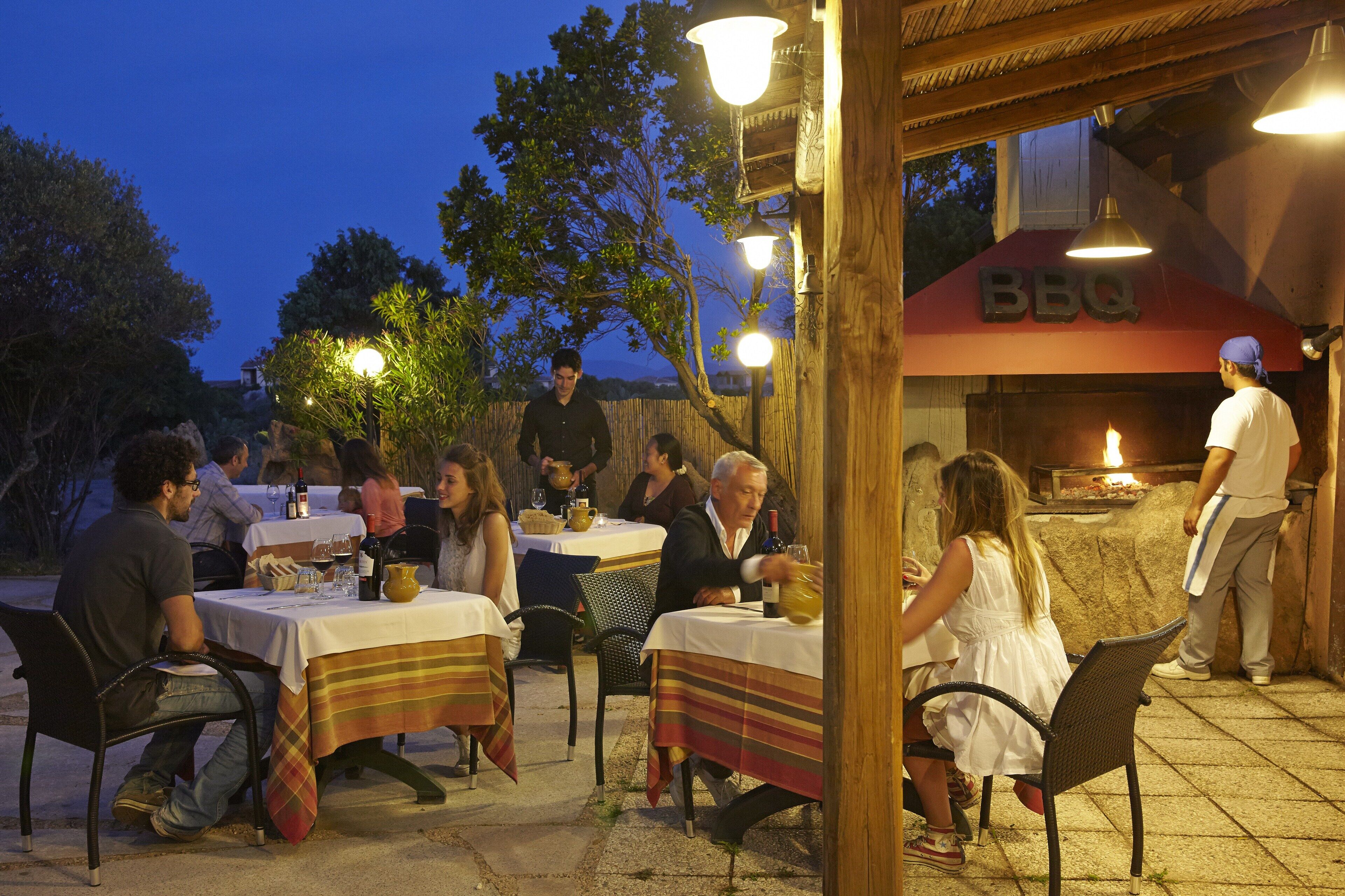 An outdoor dining area with tables and chairs, a BBQ sign, and a chef preparing food.