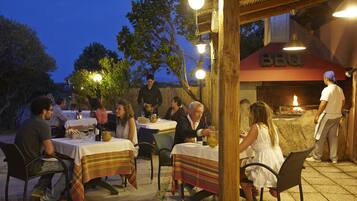 An outdoor dining area with tables and chairs, a BBQ sign, and a chef preparing food.
