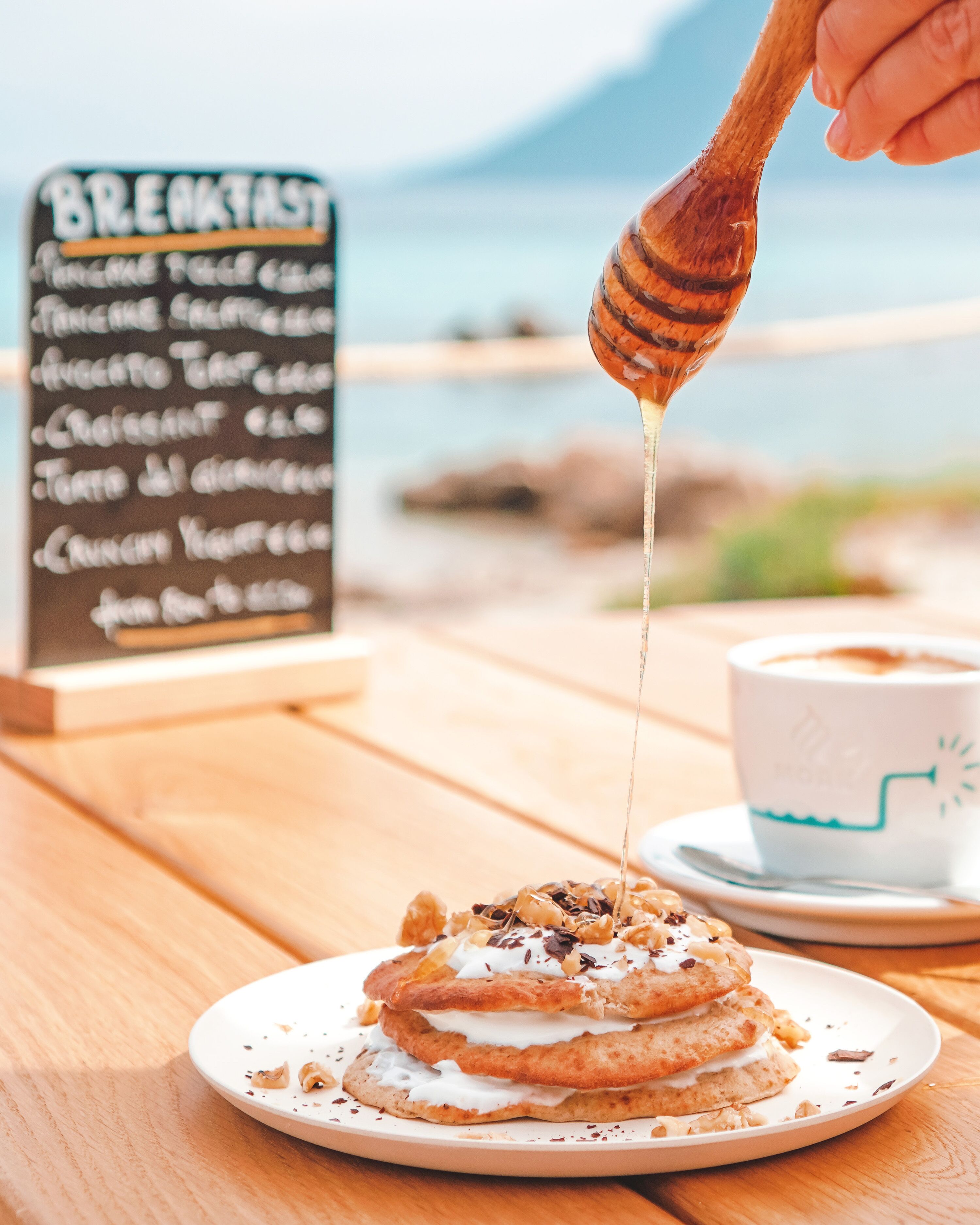 Een ontbijtsetting met een bord pannenkoeken, belegd met slagroom en siroop, een koffiekop en een menubord.