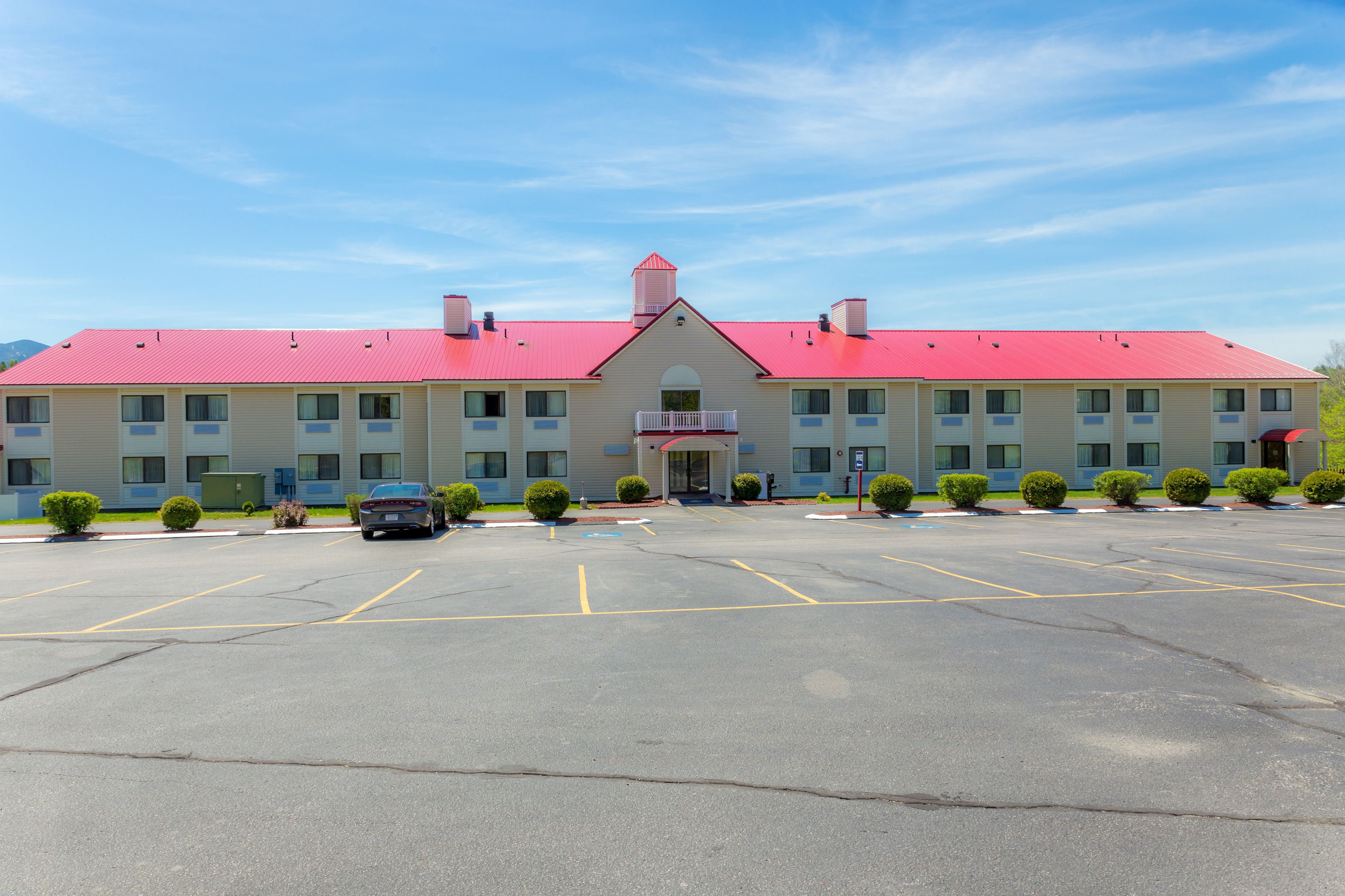 A motel with a red roof, multiple rooms, and a parking lot.