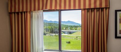 A room with a large window, striped curtains, and a view of a bridge and mountains.
