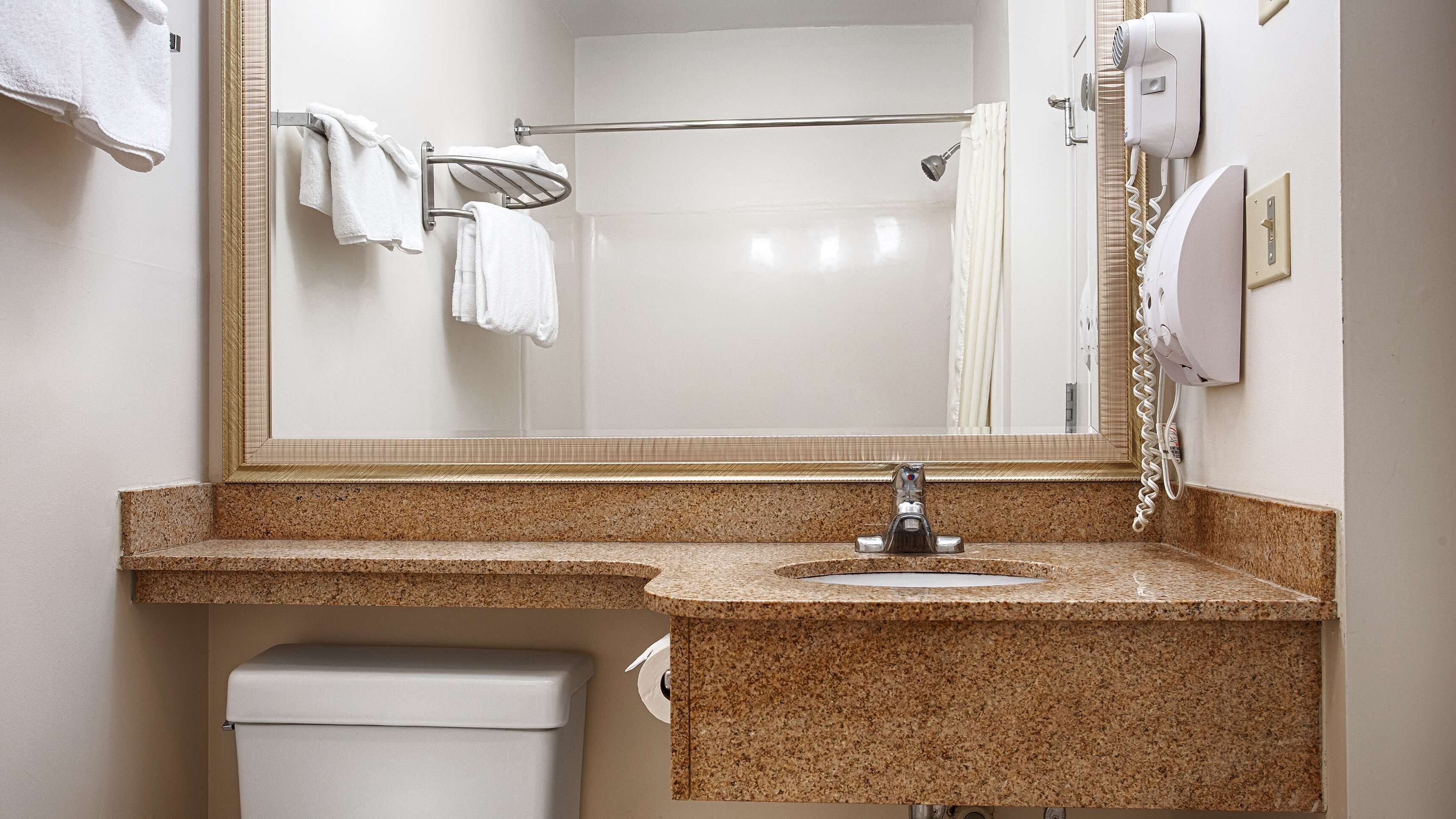 A bathroom with a granite countertop sink, a mirror, a towel rack, a shower curtain, and a hairdryer.