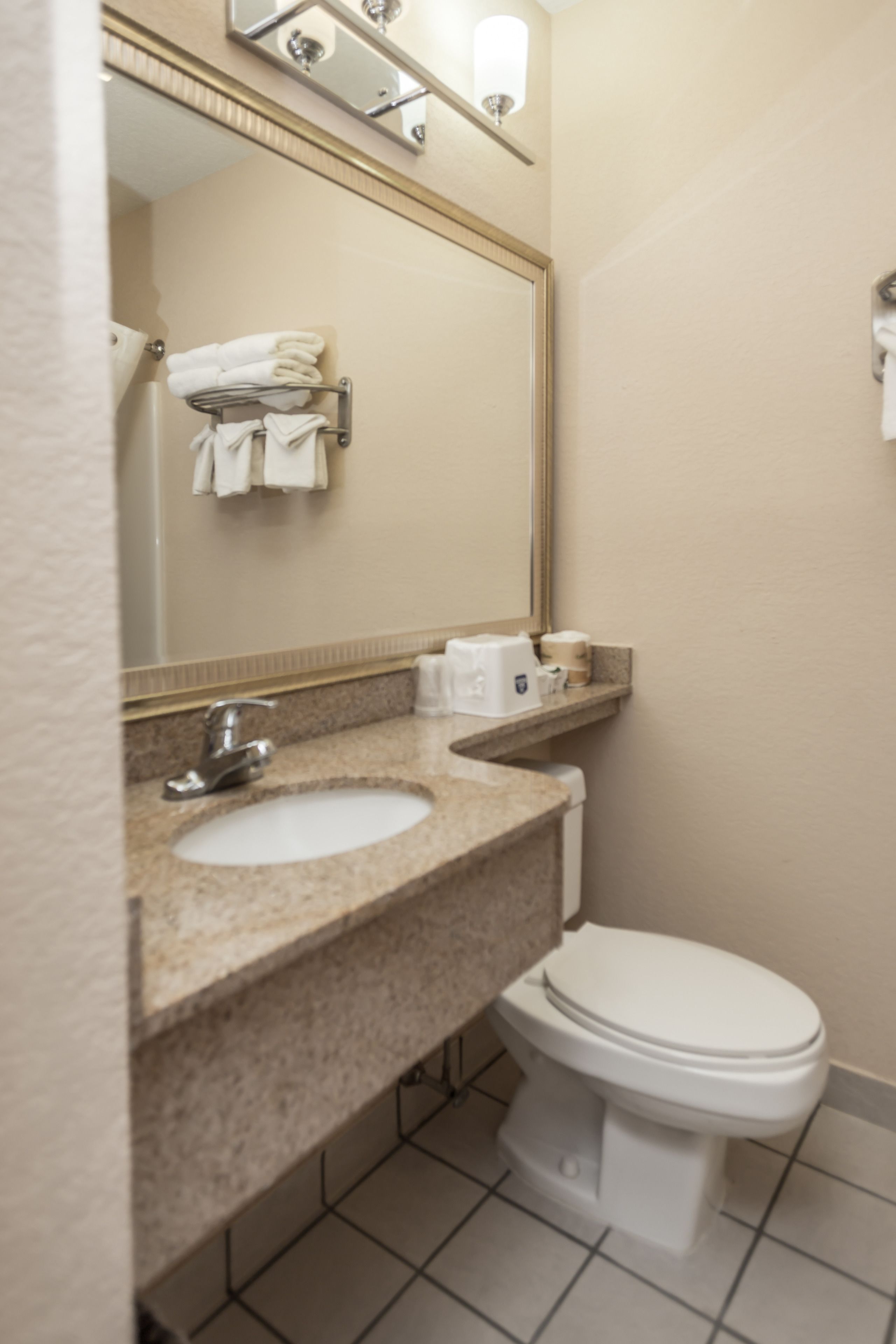 A bathroom with a sink, mirror, towel rack, toilet, and a small shelf with toiletries.