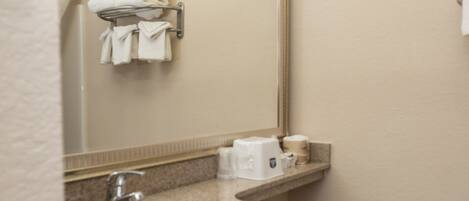 A bathroom with a sink, mirror, towel rack, toilet, and a small shelf with toiletries.