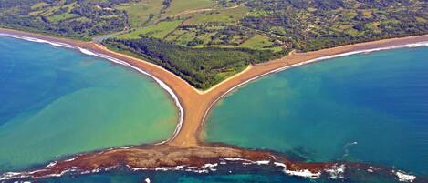An aerial view of a coastal landscape with a beach, clear waters, and a forested area.