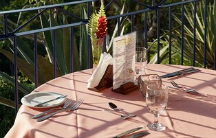 Una mesa colocada al aire libre con un menú, vasos y cubiertos.