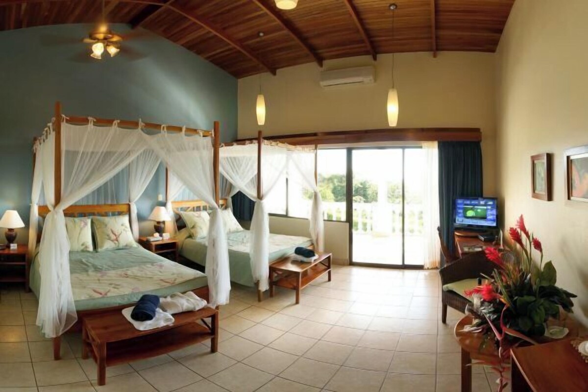 Een slaapkamer met een hemelbed, een televisie en een zithoek met een tafel en stoelen.