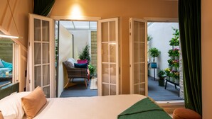 A bedroom with a bed, a green throw, and a view of an outdoor balcony with plants. - Hôtel Veryste & Spa (Paris)