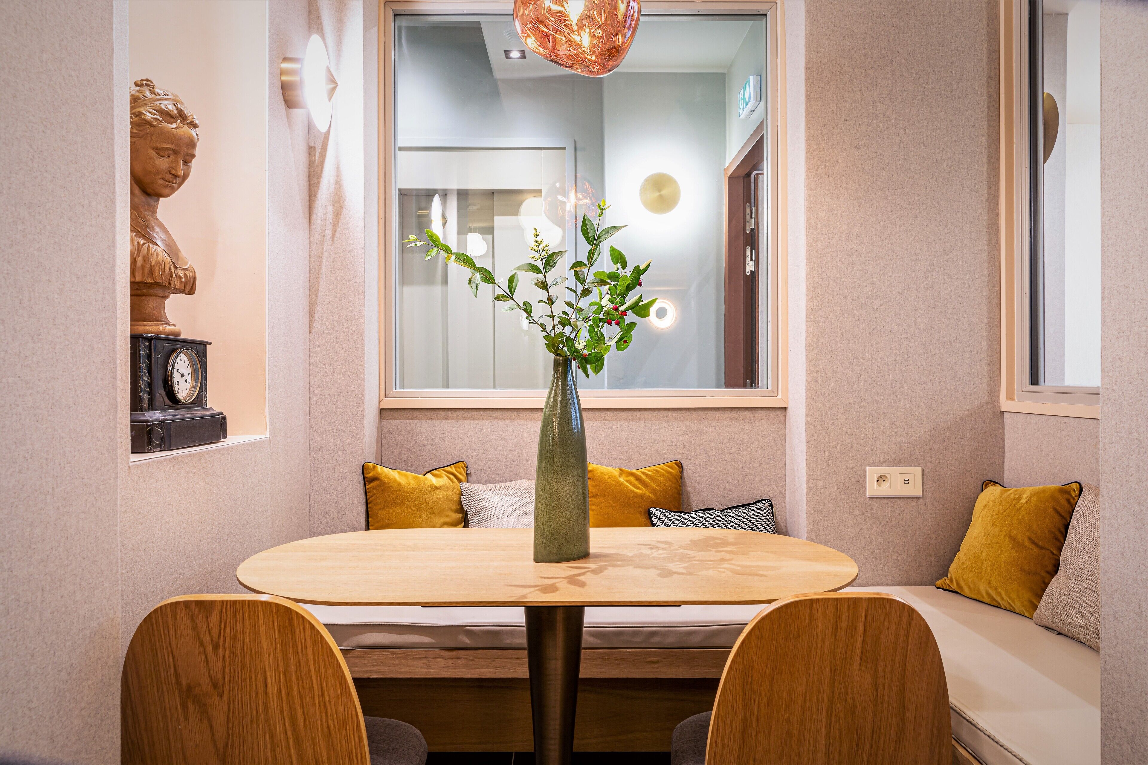 A dining area with a round table, wooden chairs, a vase with flowers, and a bench with yellow cushions.