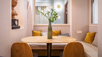 A dining area with a round table, wooden chairs, a vase with flowers, and a bench with yellow cushions.