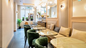A hotel lobby with round tables, green upholstered chairs, and a seating area with a sofa and cushions. - Hôtel Veryste & Spa (Paris)