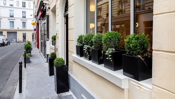 A building with a restaurant sign, a sidewalk with potted plants, and a street view. - Hôtel Veryste & Spa (Paris)