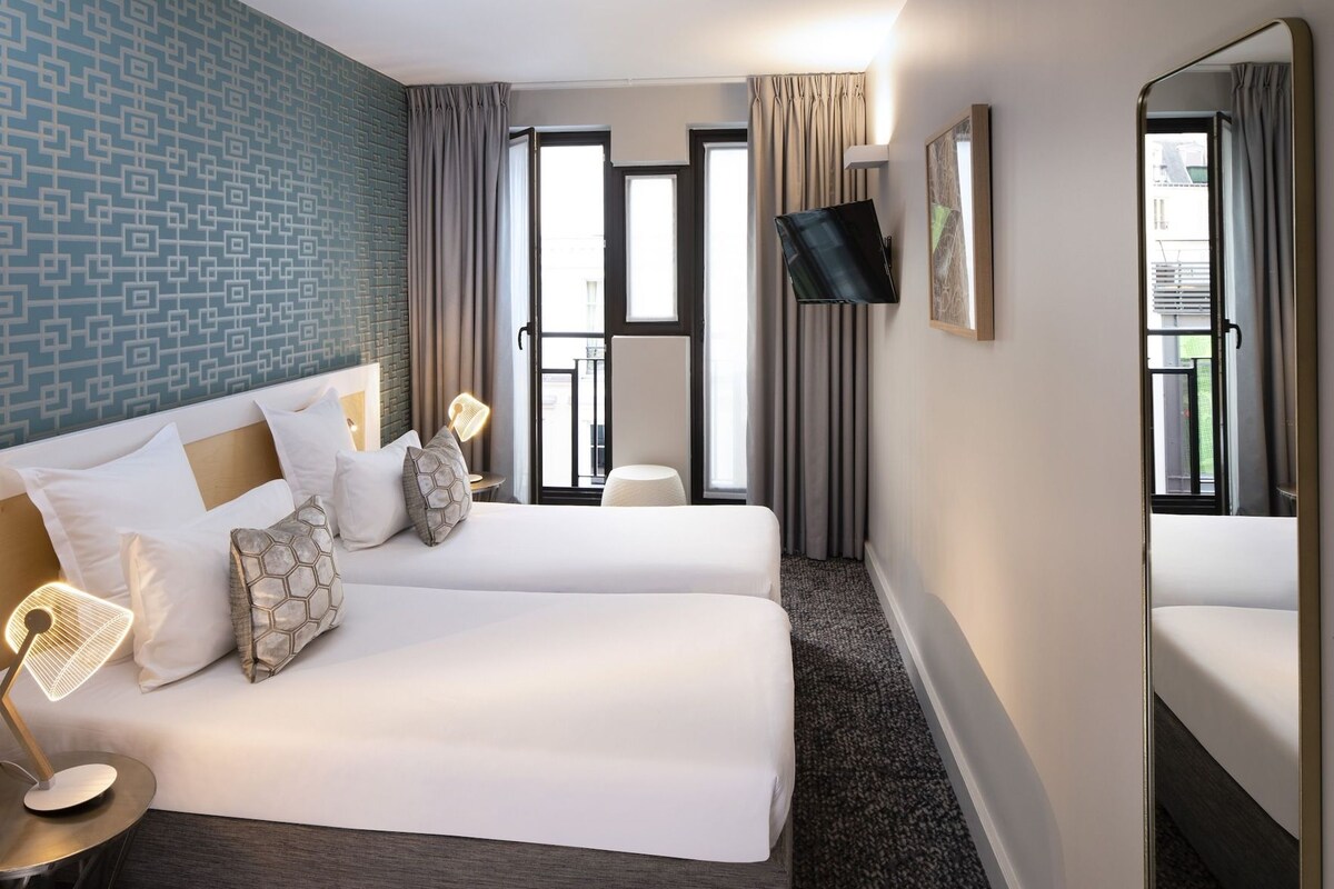 Habitación de hotel con dos camas, televisión, una mesita y ventana con cortinas.