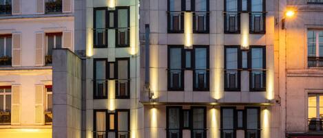 A modern hotel building with multiple floors, large windows, and illuminated exterior lighting.
