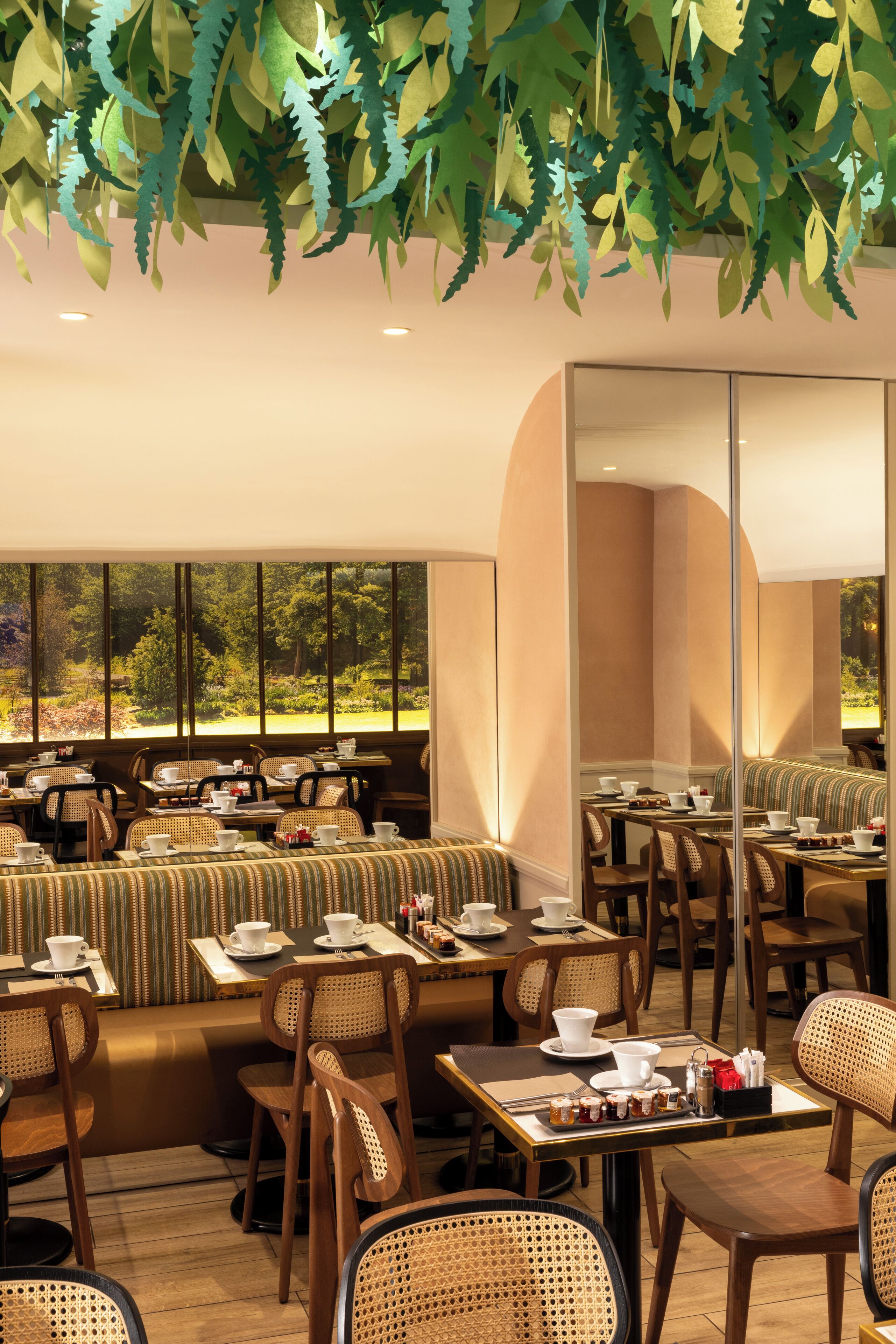 A restaurant with wooden furniture, large windows, and hanging paper leaves.