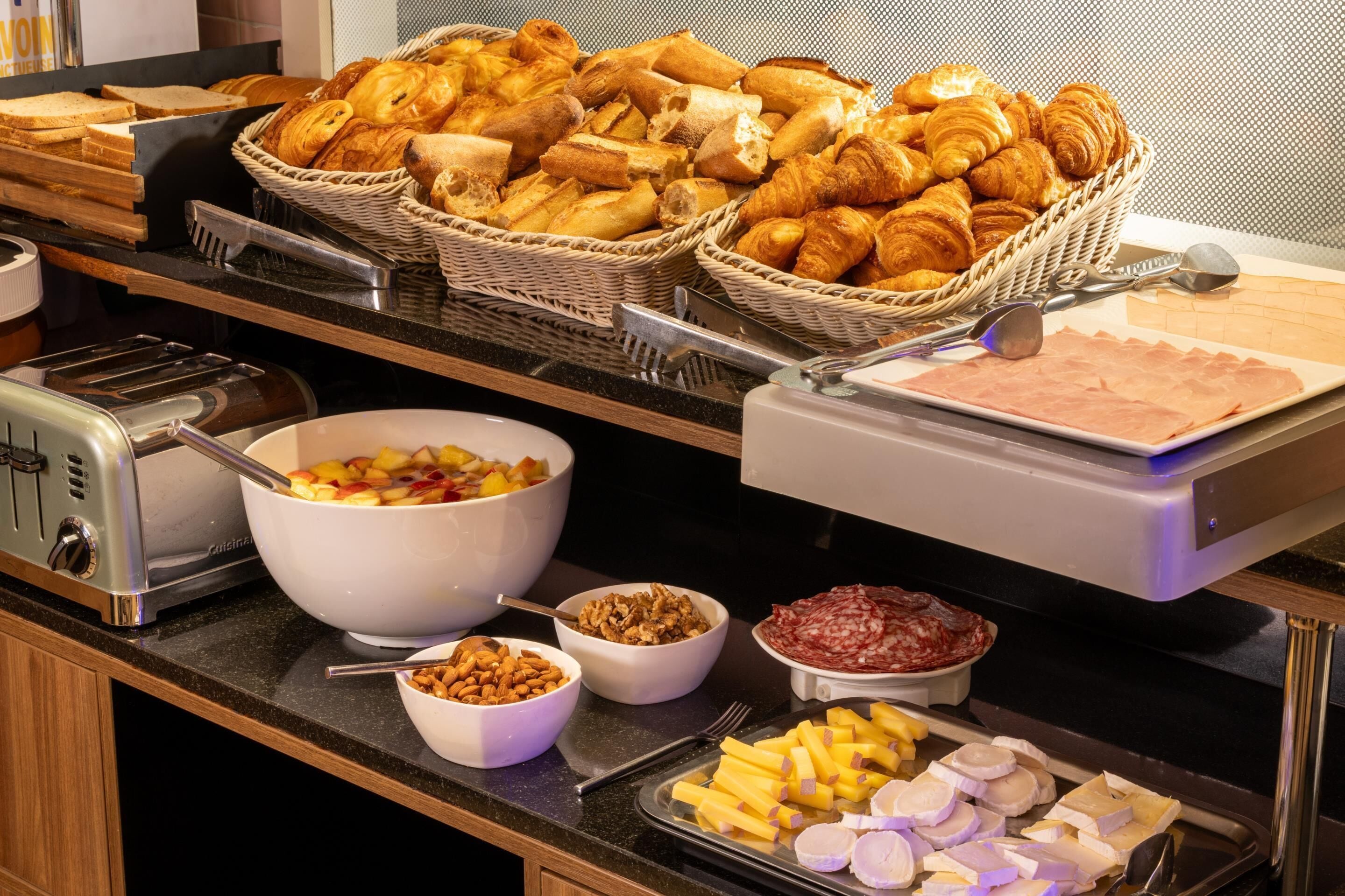 A buffet with various food items including bread, pastries, fruits, and cheeses.
