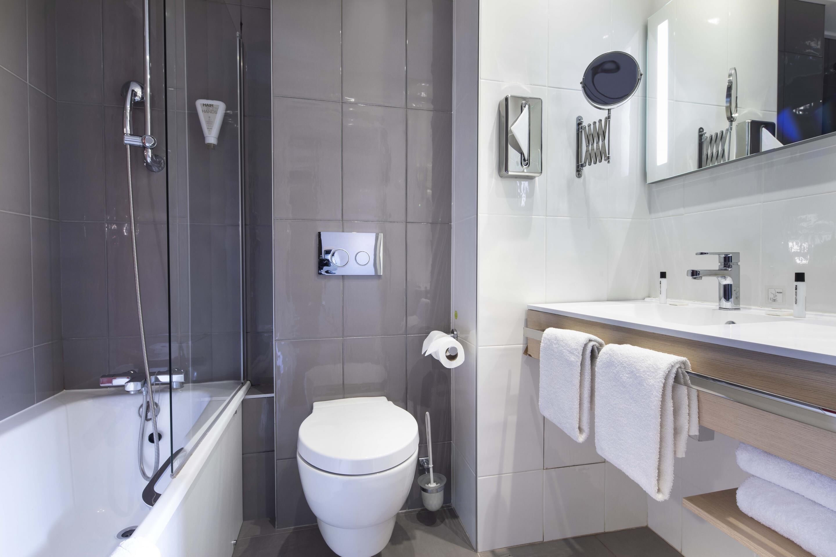 A modern bathroom with a bathtub, toilet, and a vanity with a mirror and towel rack.