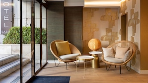 A modern hotel lobby with glass doors, wicker chairs, a round table, and a decorative wall. - Hotel Paris Bastille (Paris)