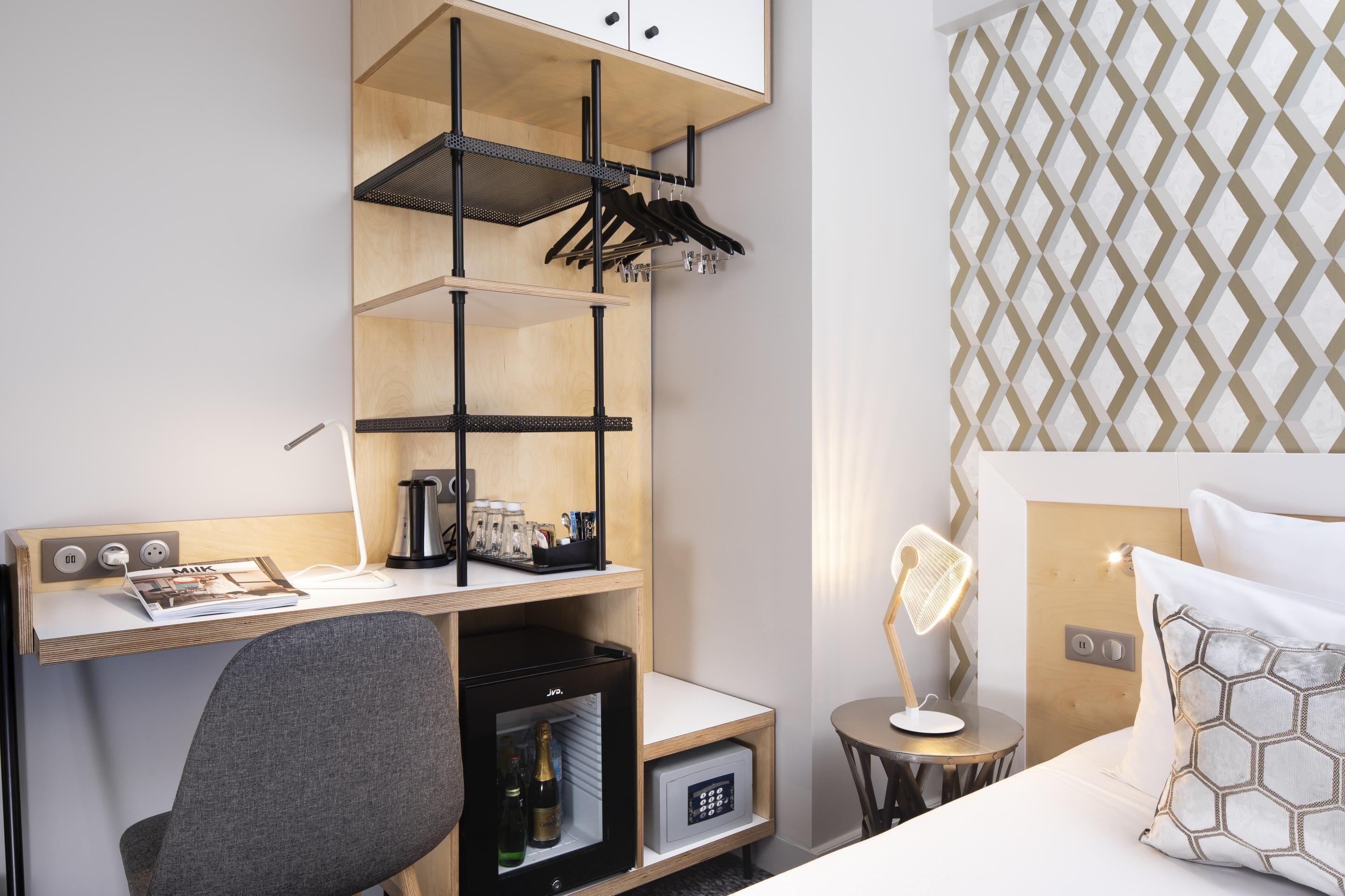 Habitación de hotel con escritorio, minibar, cama con cabecera y pared con diseño.