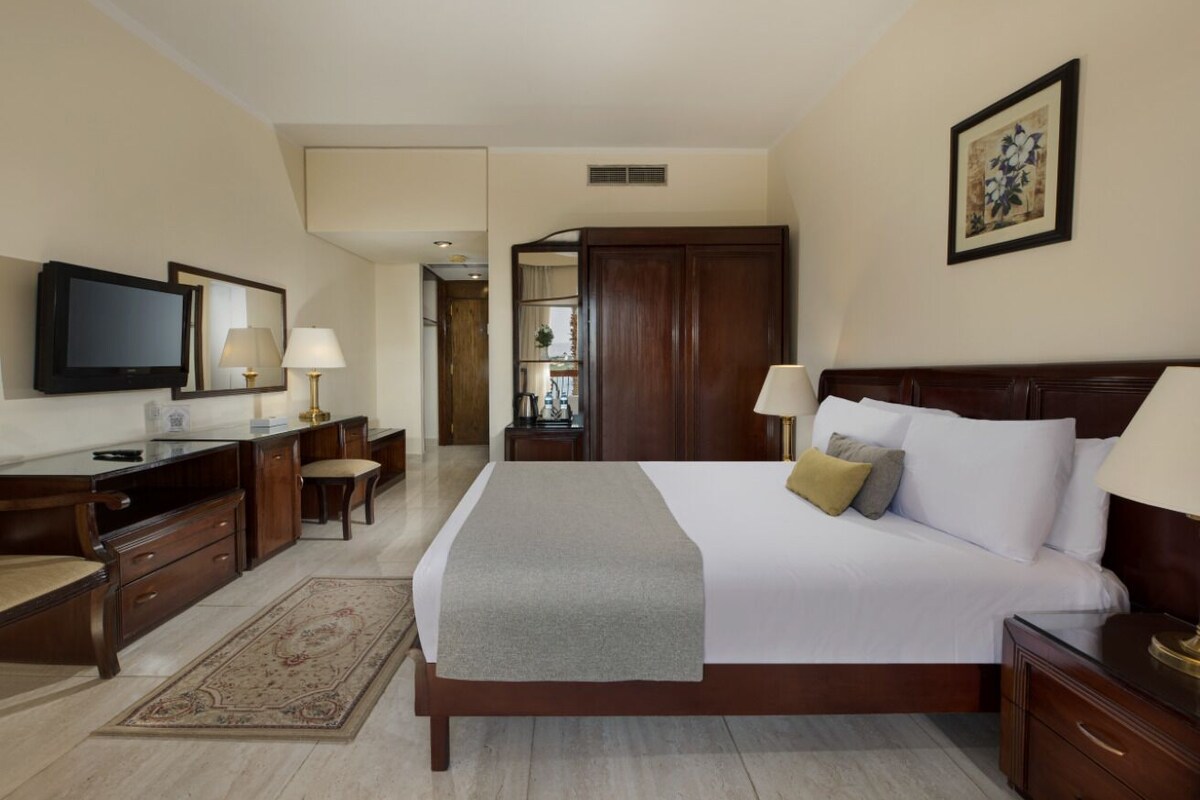 Une chambre d’hôtel avec un grand lit, un bureau avec une chaise, une télévision et une armoire.