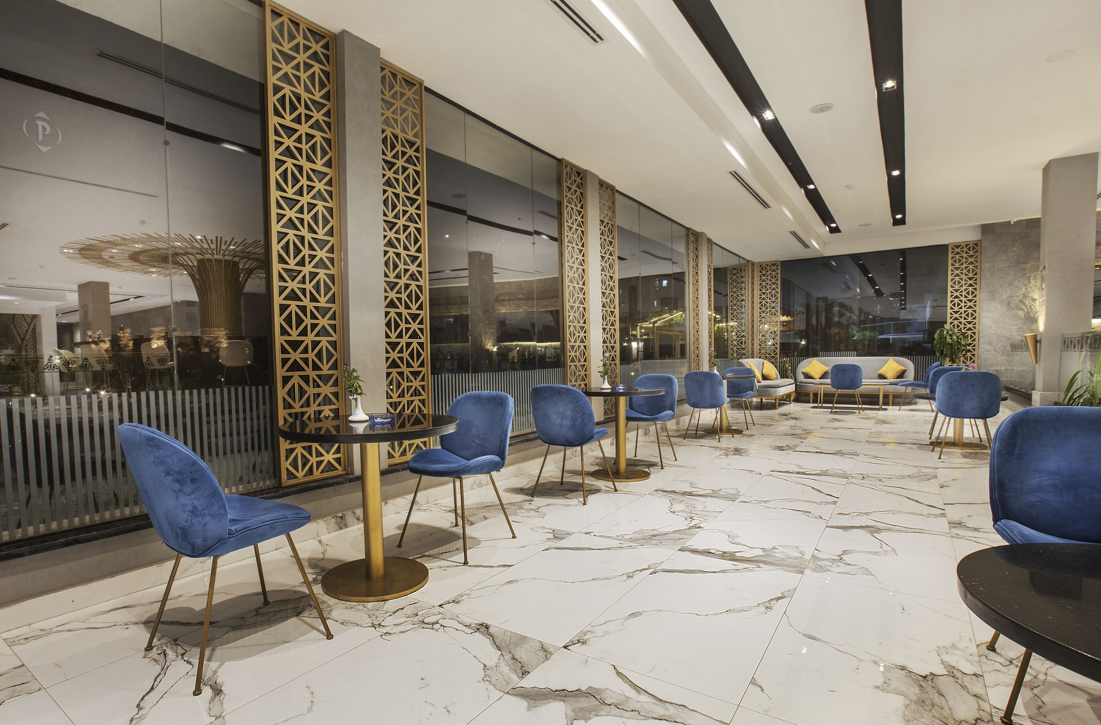 A modern lobby with marble flooring, blue chairs, and a seating area with yellow cushions.