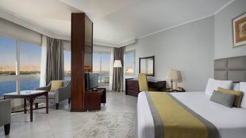 A hotel room with a bed, a desk, a chair, a TV, and a view of the water.