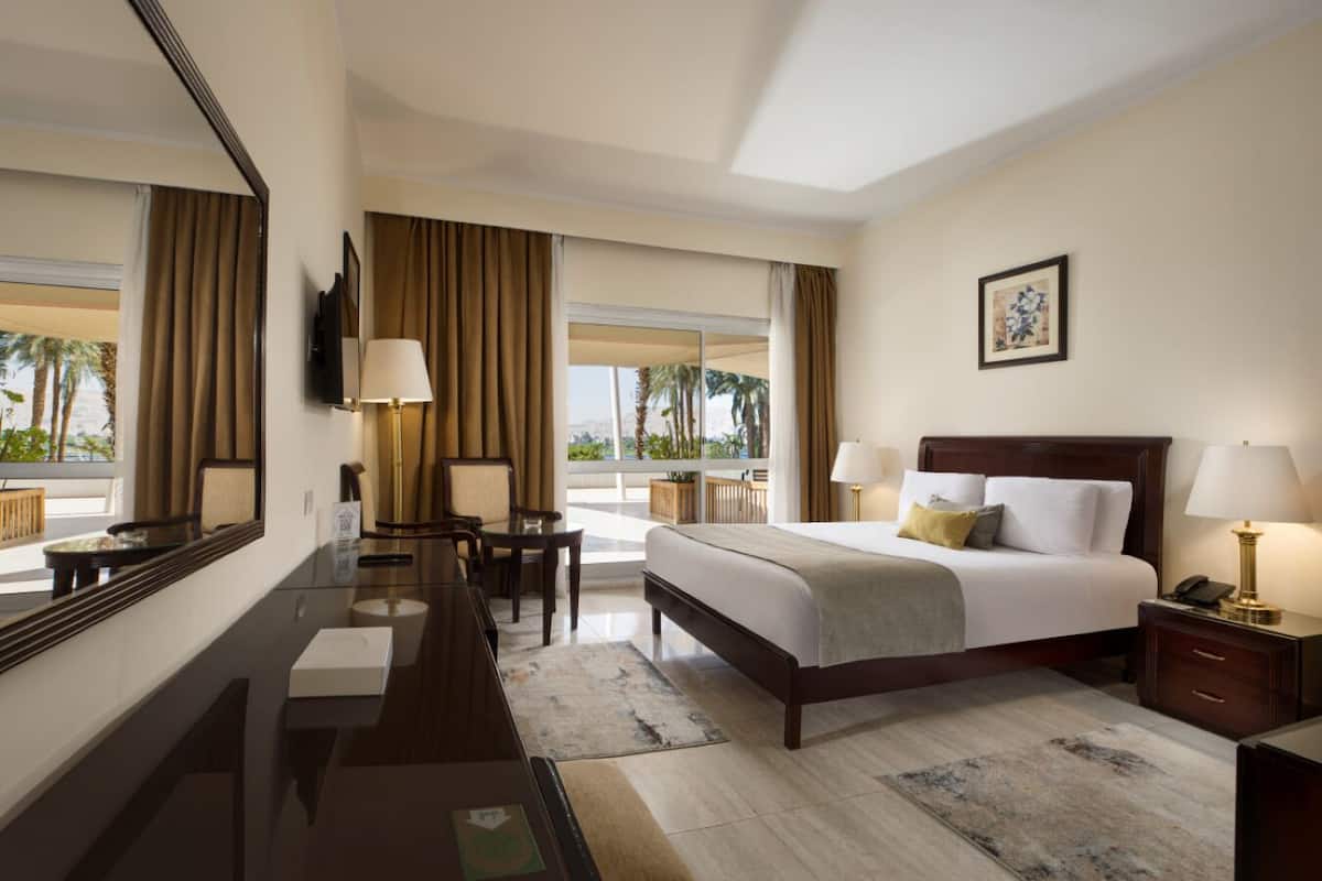 Habitación de hotel con una cama grande, un escritorio, una silla, un televisor y una ventana con cortinas.