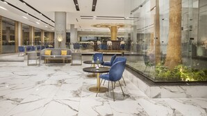 A modern lobby with marble flooring, blue chairs, a round table, and a glass enclosure with a tree. - Pyramisa Hotel Luxor (Luxor)