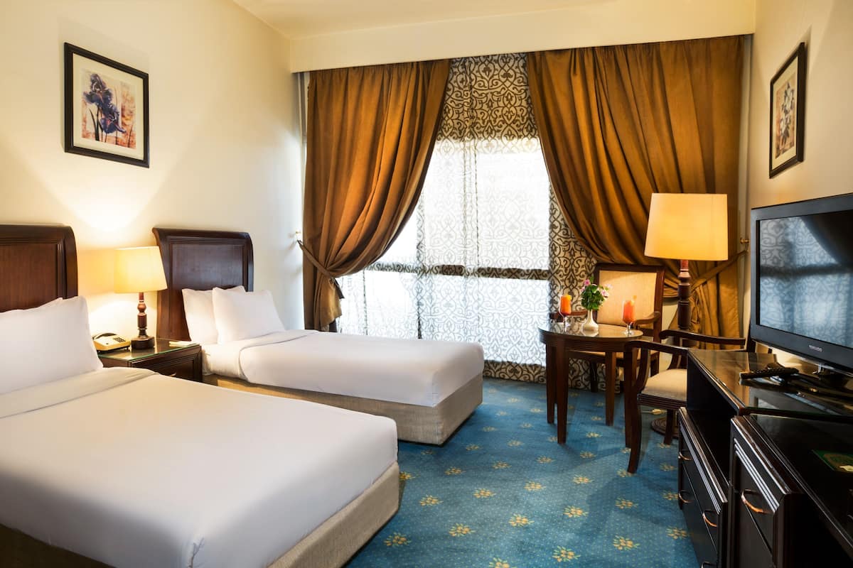 Habitación de hotel con dos camas, un escritorio con una silla, televisión y ventana con cortinas.