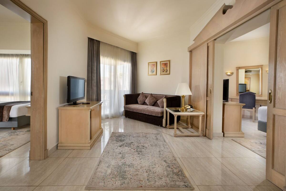 Una habitación de hotel con sofá, televisión sobre un mueble bajo, lámpara y alfombra.