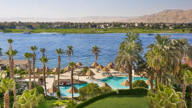 A resort with a pool, palm trees, and a view of a river and mountains. - Pyramisa Hotel Luxor (Luxor)