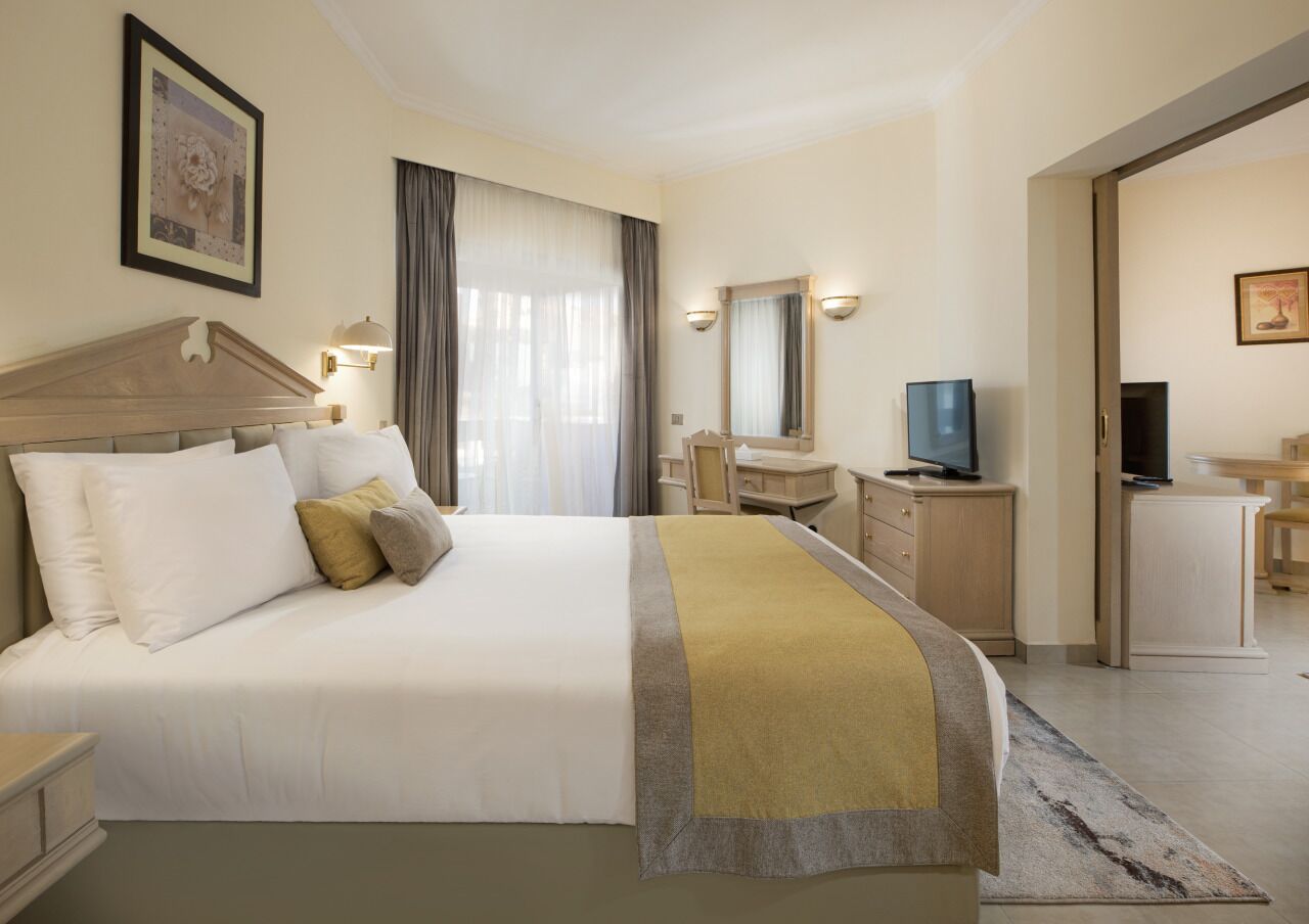 A hotel room with a large bed, a desk, a chair, a television, and a mirror.