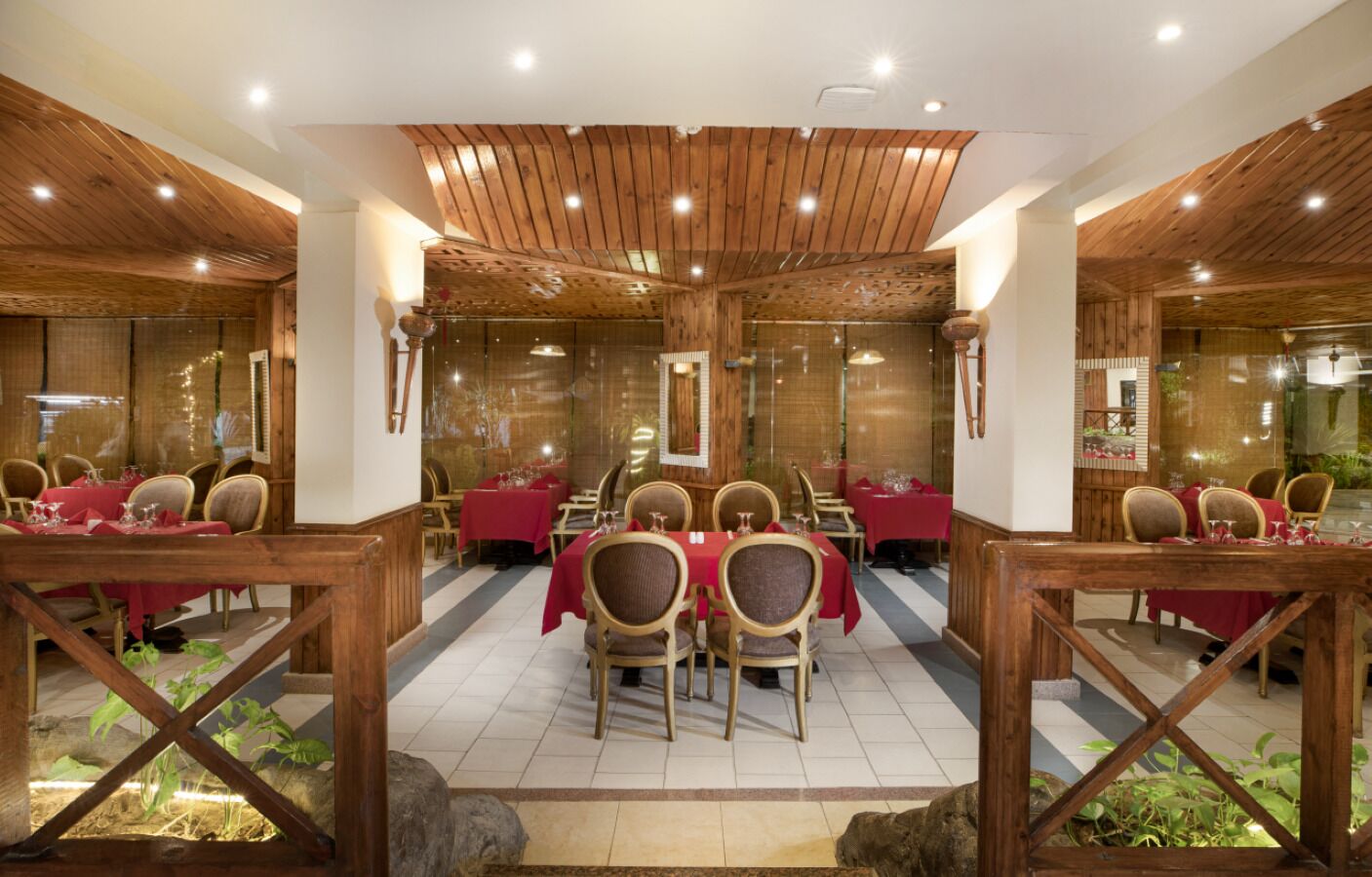 A restaurant with wooden ceiling and walls, red tablecloths, and wooden chairs.