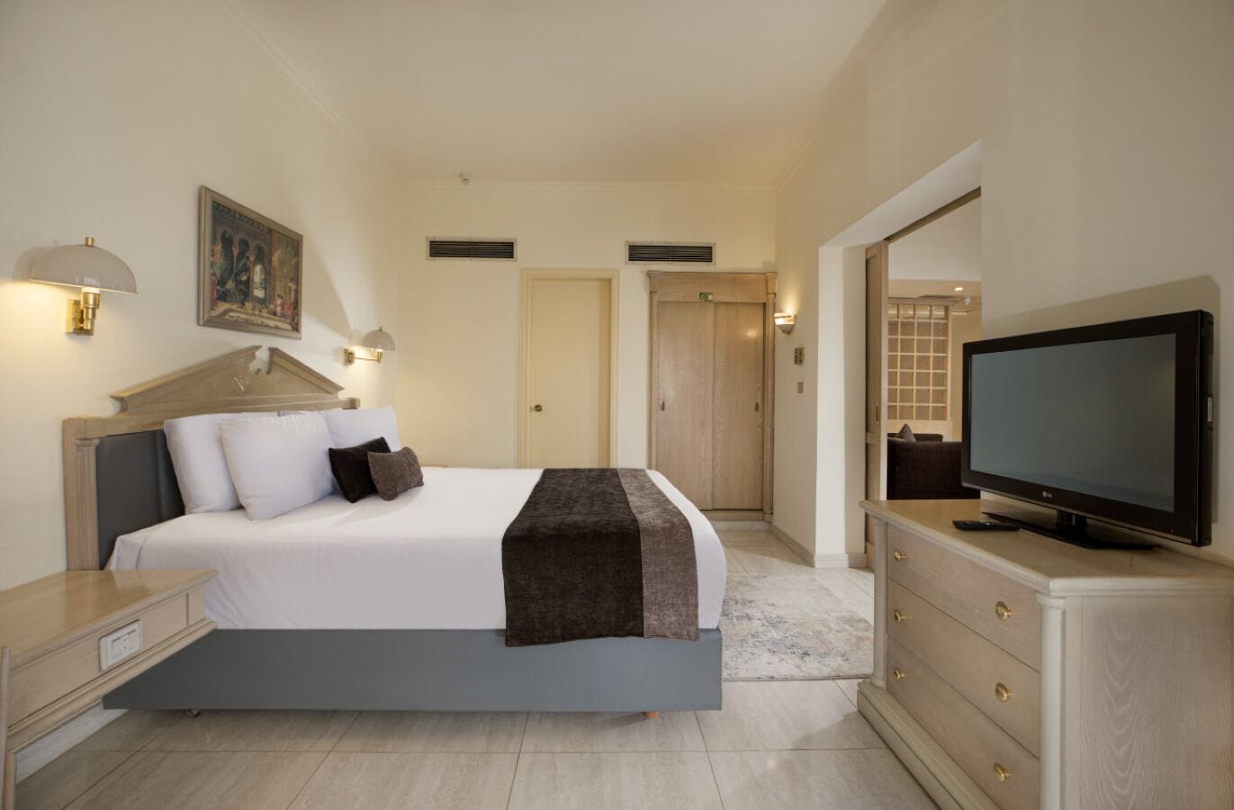 A modern hotel room with a large bed, a television, and a desk with drawers.