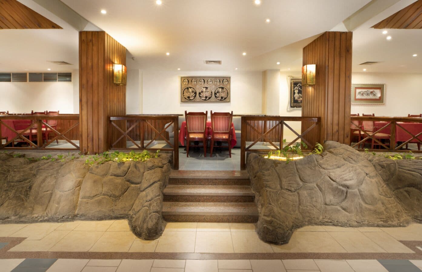 Restaurante com entrada em parede de pedra, painéis de madeira e cadeiras vermelhas.