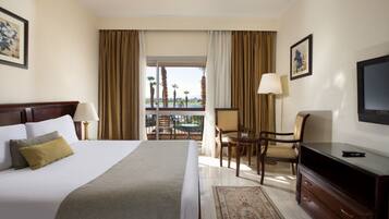 Habitación de hotel con una cama grande, un escritorio con silla, televisor y un balcón con vista a palmeras.