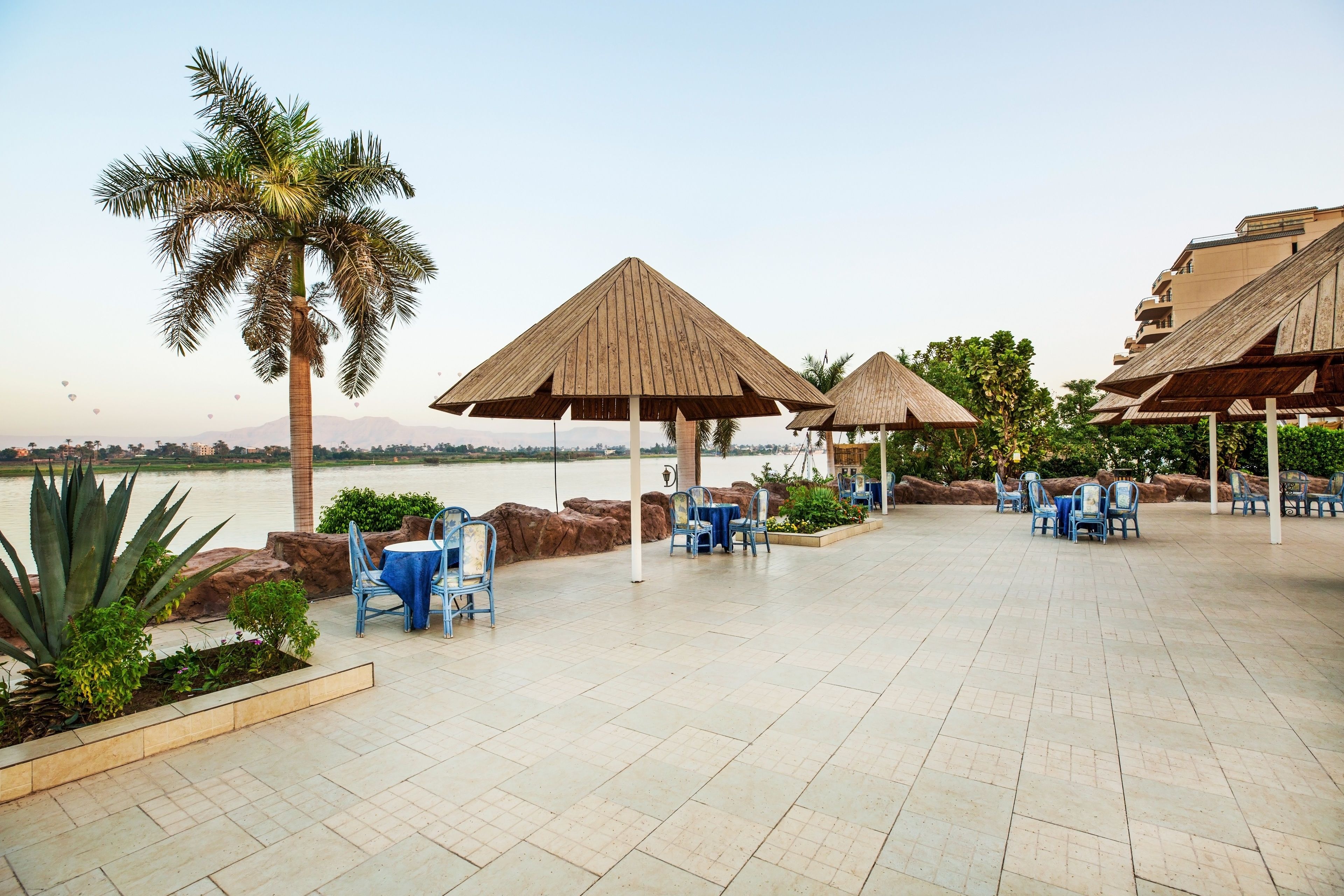 A terrace with thatched umbrellas, outdoor seating, and a view of the water.