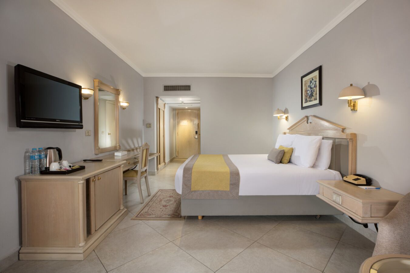 A hotel room with a bed, bedside table, TV, desk, and a mirror.