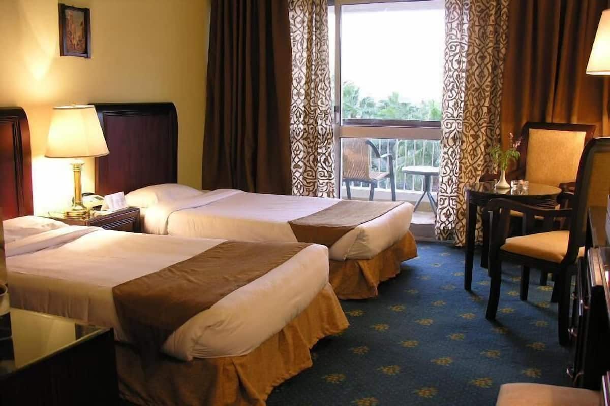Habitación de hotel con dos camas, un escritorio, una silla y un balcón con vistas.