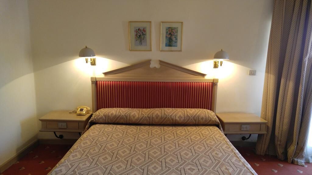 A hotel room with a bed, two bedside lamps, a telephone, and two framed pictures on the wall.
