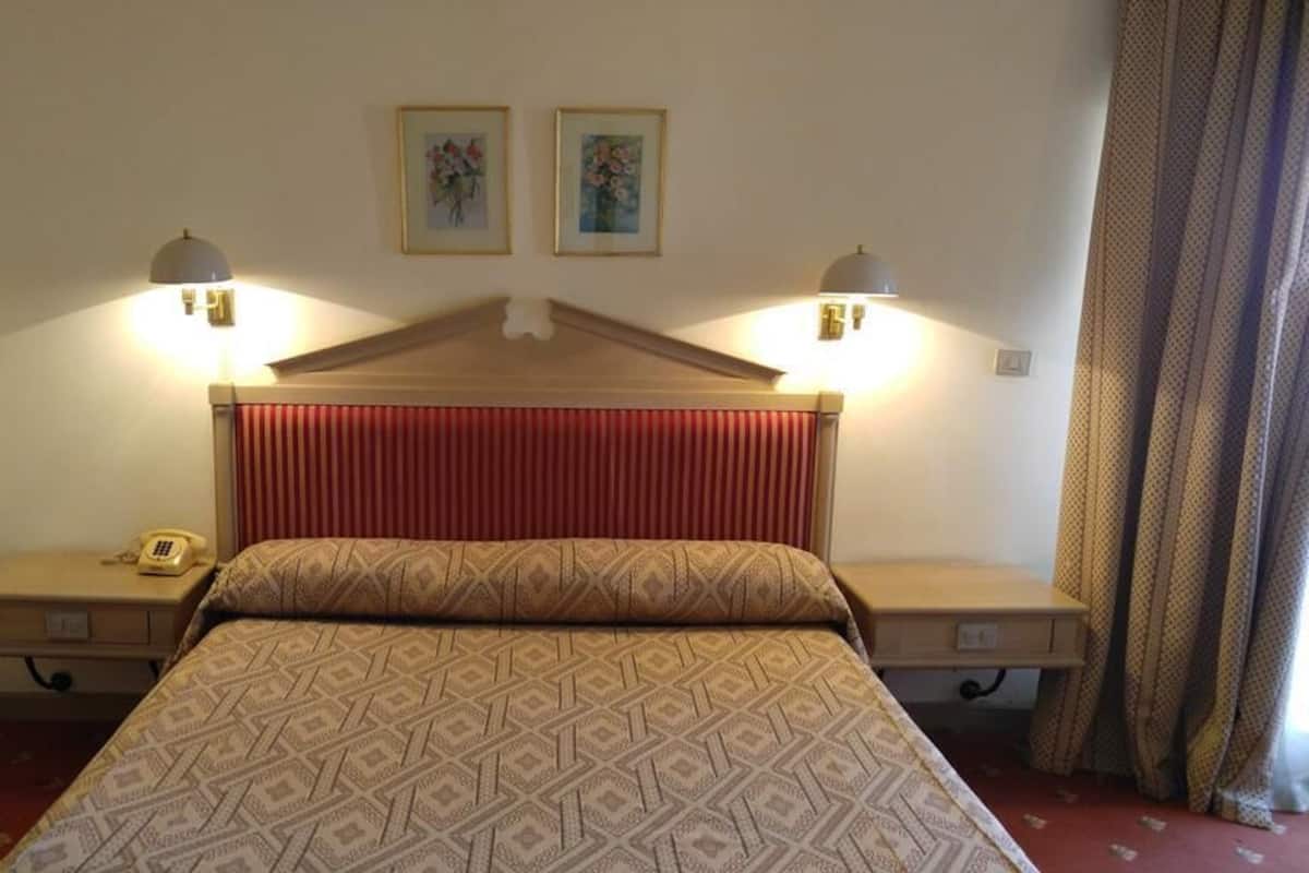 Una habitación de hotel con una cama, dos lámparas de noche, un teléfono y dos cuadros en la pared.