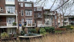 A row of brick townhouses with balconies, a small pond, and overgrown vegetation. - Hotel Oorsprongpark (Utrecht)