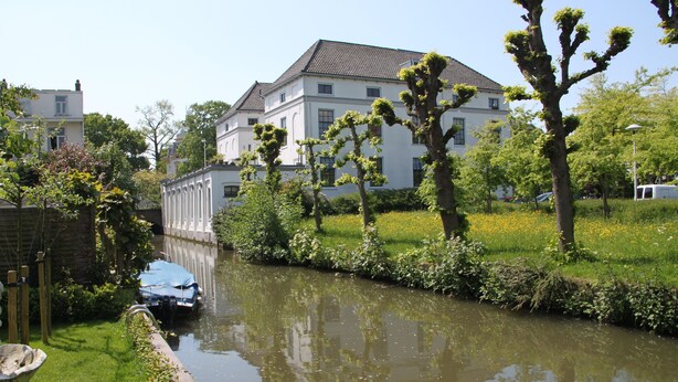 A canal with a building in the background, surrounded by greenery and trees. - Hotel Oorsprongpark (Utrecht)