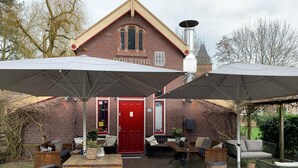 A brick building with a red door, outdoor seating area with tables and chairs, and umbrellas providing shade. - Hotel Oorsprongpark (Utrecht)