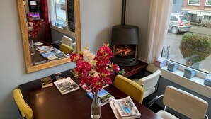 A dining area with a table, chairs, a vase with flowers, a fireplace, a mirror, and a window with a view of the street. - Hotel Oorsprongpark (Utrecht)