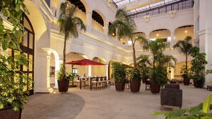 Une cour intérieure spacieuse, dotée de plusieurs coins salon, de plantes en pot et d’un parasol rouge.