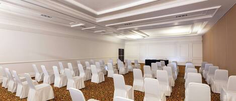 A conference room with rows of white chairs and a podium at the front.