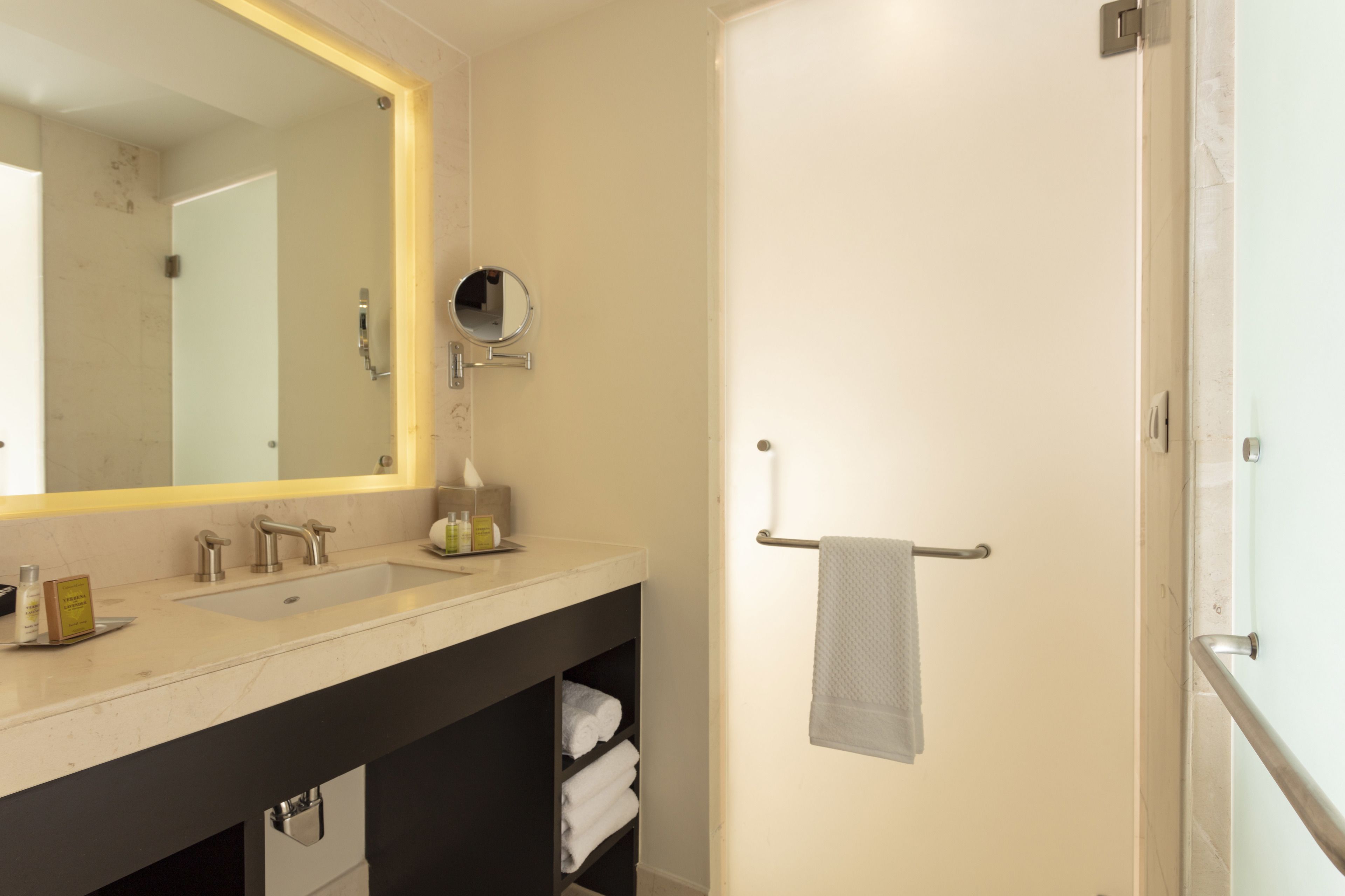 Un baño moderno con un espejo grande, dos lavamanos, un perchero para toallas y un box de ducha de vidrio.