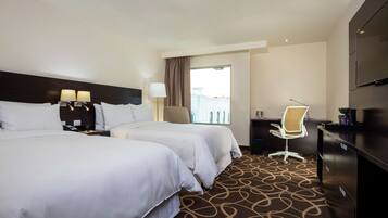 A hotel room with two beds, a desk, a chair, a TV, and a window with a view.